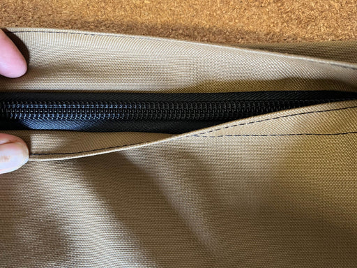 Close-up of a tan Hay Pillow slow feeder canvas zipper pouch being opened by fingers, showing a YKK black zipper and the woven canvas fabric texture.