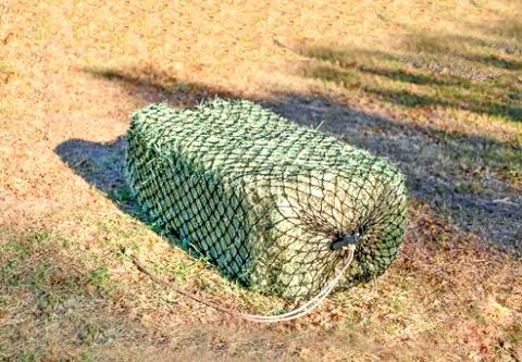 West coast size hay bale net for slow feeding horses filled with a large bale of grass hay and laying on the ground.